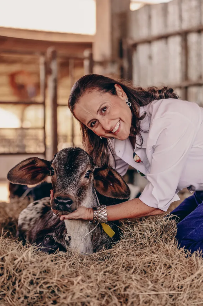 Mulher com o rosto encostado na cabeça de uma bezerra deitada no feno, sorrindo